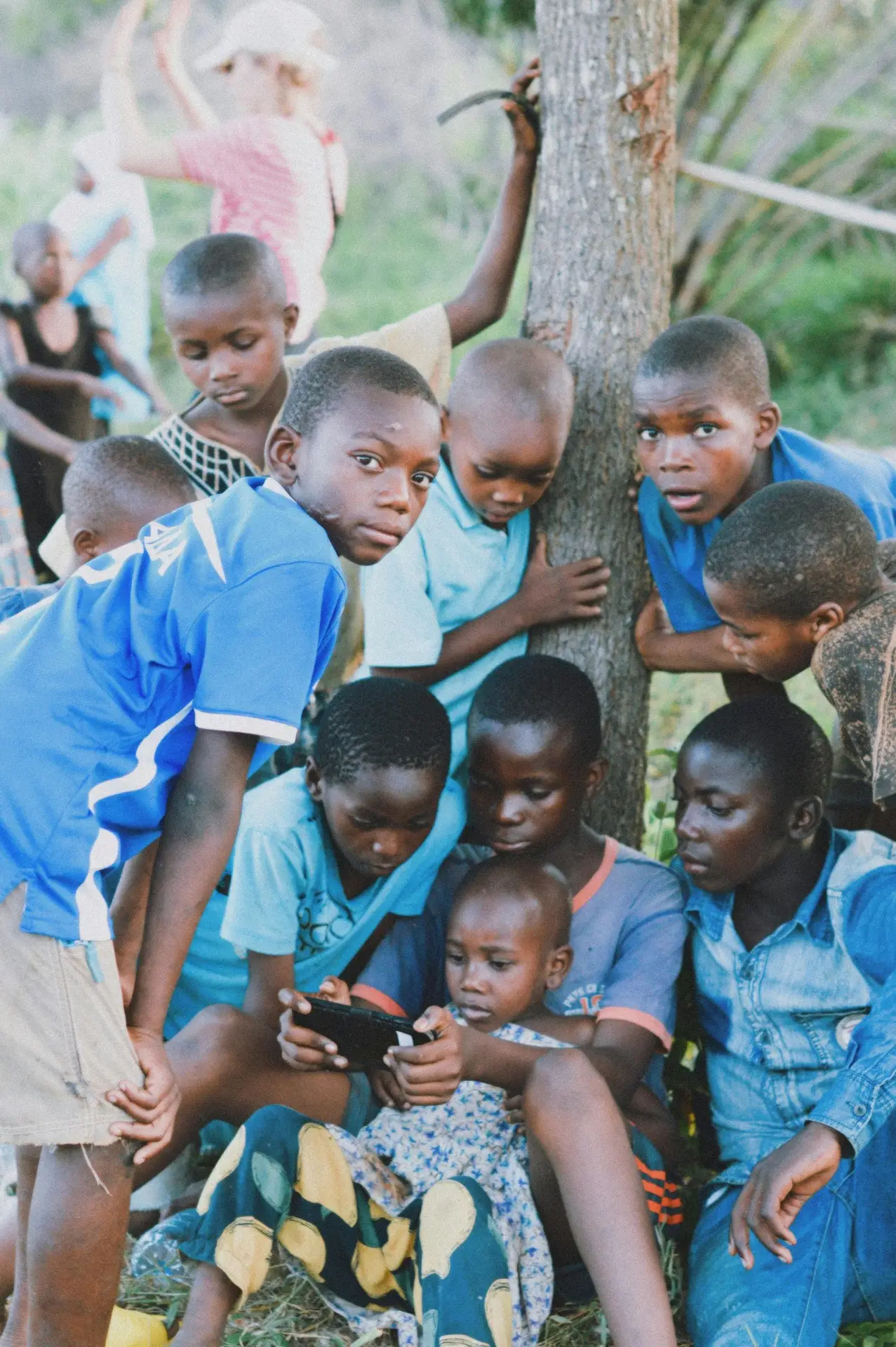 A group of African children gathered outside, engaged with a device in Tanzania.